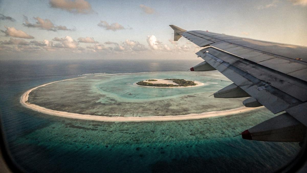 Aircraft wing above turquoise water on the approach to a Maldives atoll