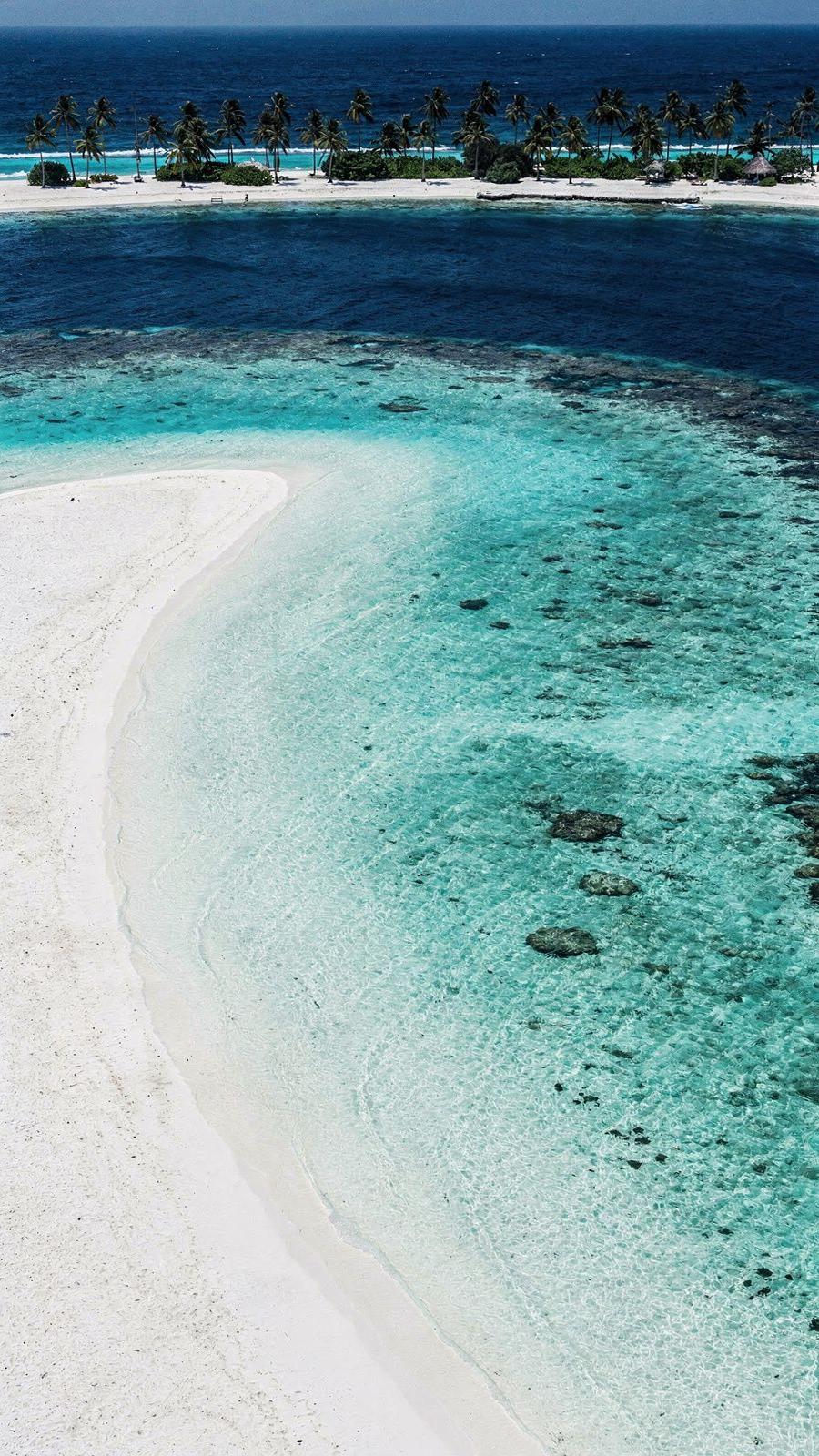 Elevated view of a Maldivian atoll coastline with pale sand meeting a shallow turquoise lagoon